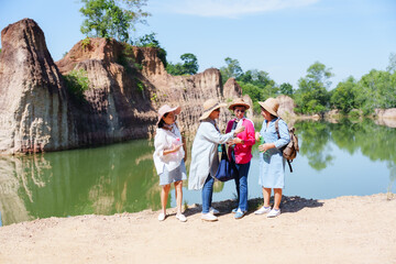 Group of four Asian female friends, mature adults in casual attire and hats, conversing by serene...