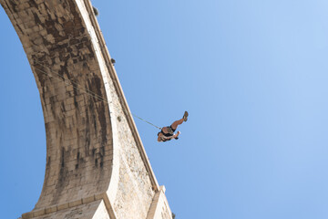 Low angle view of a person swinging after bungee jumping from a historic stone bridge. Adventure...
