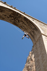 Low angle view of a person bungee jumping from a historic stone bridge. Adventure sports concept