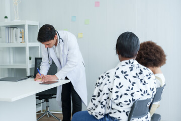 Fototapeta premium Doctor in white attire pens notes on clipboard, consulting patient seated opposite, clinic's interior visible. Health specialist scribbles on notepad, engaging with seated client
