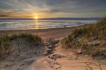 A footpath through the dunes leads to the beach where enjoying the sunset is a pleasure. Two people...