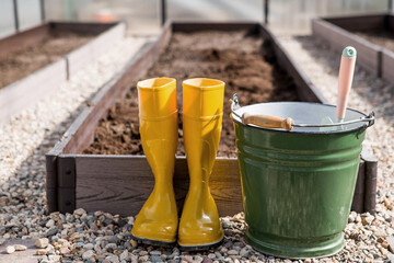 Yellow rubber boots, a bucket and a small shovel in the new greenhouse. The concept of spring...