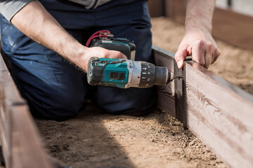 A man holds a battery-powered screwdriver and collects new beds from WPC into a greenhouse made of...