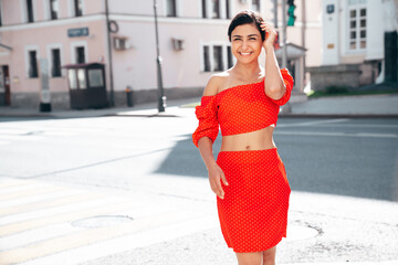 Young beautiful smiling hipster woman in trendy summer red top and skirt clothes. Carefree female posing in the street at sunny day. Positive model outdoors at sunset. Cheerful and happy