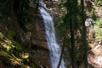 A high waterfall flows down among the rocks and trees in the forest