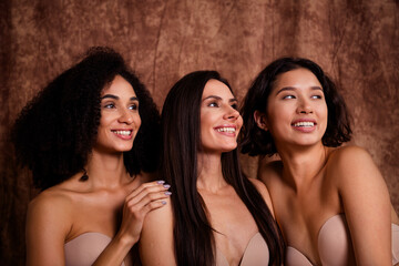 Portrait of three smiling young girls looking empty space body positivity promotion isolated on brown color background