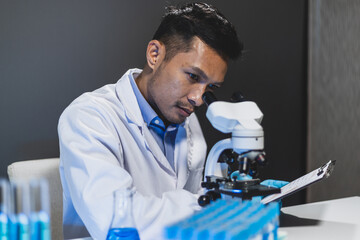 Doctor or scientist in laboratory looking at microscope and writing down experimental results.