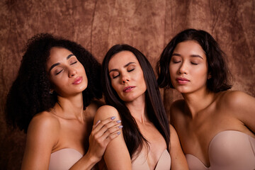 Portrait photo of three young models in brassieres the closed eyes and dreaming isolated on brown...