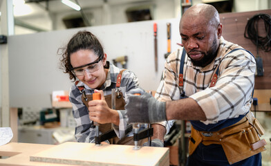 Female Latin carpenter and multiracial colleague working in carpenter's shop repair wood furniture....