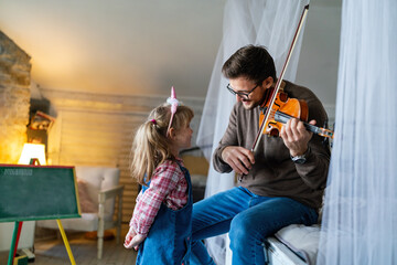 Happy single father smiling at his daughter while playing a violin at home.
