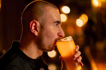 Fototapeta premium close-up on a wooden bar table guy drinks from a glass of light beer warm lighting light