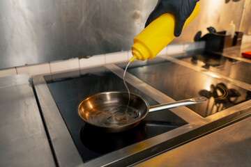 in professional kitchen the chef pours oil into a small frying pan on the stove