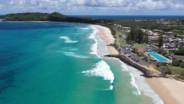 Drone flying along coast with view of surrounding buildings, waves, beach and mountains in distance