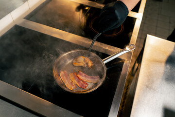 top shot close-up on professional stove on a small frying pan the chef turns the bacon with tweezers