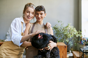 Two women in tender embrace with hen at an art studio.