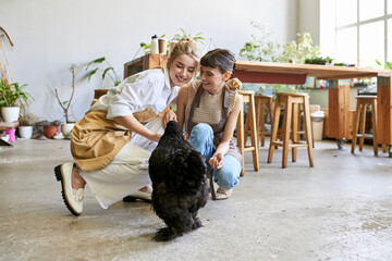 Two women tenderly kneels next to a black hen in an art studio