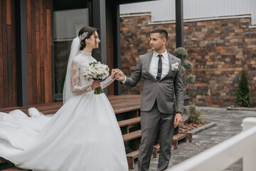 Fototapeta premium A bride and groom are standing outside of a building, with the bride holding a bouquet and the groom wearing a tie