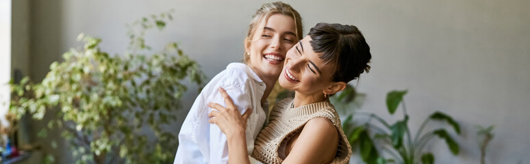 Fototapeta premium Two women, one blonde and one brunette, stand side by side in an art studio, sharing a loving moment.