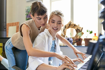 Lesbian couple passionately playing piano in art studio.