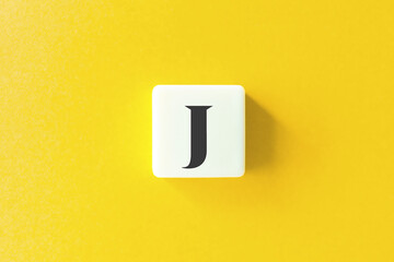 Capital Letter J. Text on Block Letter Tiles against Yellow Background.