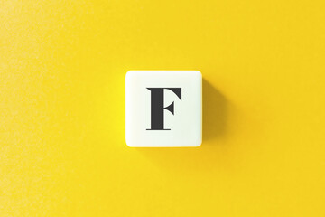 Capital Letter F. Text on Block Letter Tiles against Yellow Background.