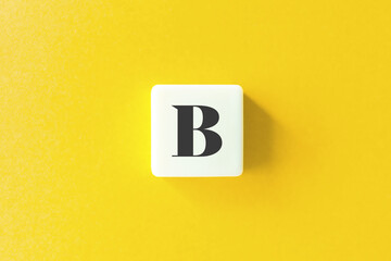Capital Letter B. Text on Block Letter Tiles against Yellow Background.