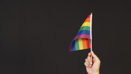 Hand is hold Rainbow pride flag on black ackground.