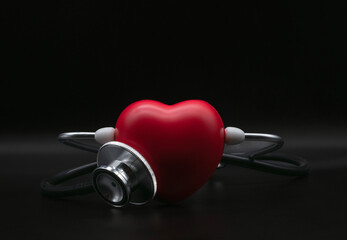 Red heart shape exercise ball with doctor physician's stethoscope on black background, hospital...