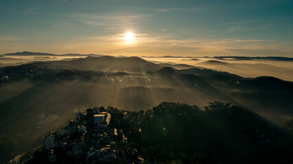 Aerial view of Da Lat at sunrise, showcasing mist-covered buildings amidst lush mountains, under a...