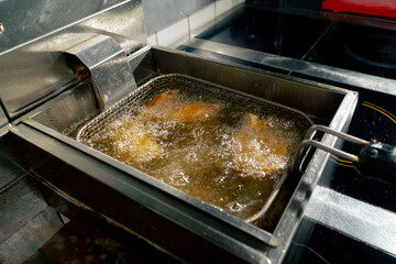 close-up in a professional kitchen frying chicken wings in oil in a deep fryer
