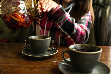 A woman carefully pours hot tea into a cup placed on a wooden table.