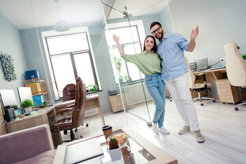 Photo of two business people stand together in modern office raise hands invite new workers