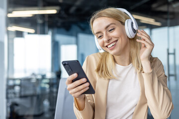 Smiling woman enjoying music on headphones in modern office
