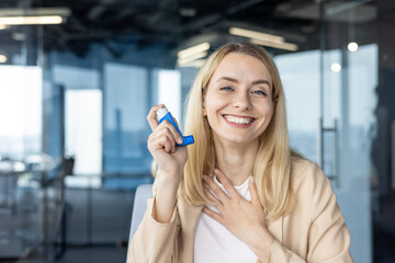 Young woman smiling in office holding a blue inhaler