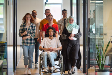 A diverse group of young business people congregates within a modern startup's glass-enclosed...