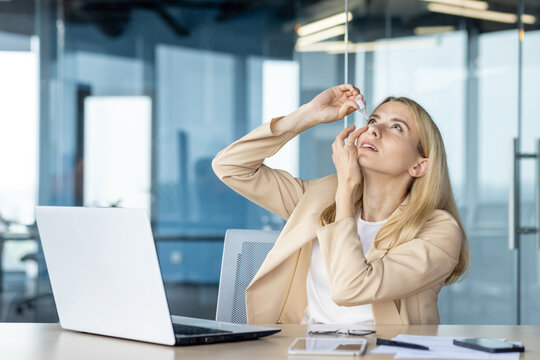 Businesswoman applying eye drops at modern office desk