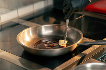 close-up in a professional kitchen the chef uses a knife to distribute oil in a frying pan