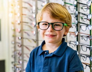 Portrait of proud young blond boy wearing kid glasses in a optician shop for child