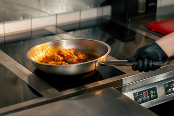 close-up of chicken wings being fried in sauce in frying pan in a professional kitchen