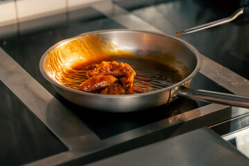 close-up of chicken wings being fried in sauce in frying pan in a professional kitchen