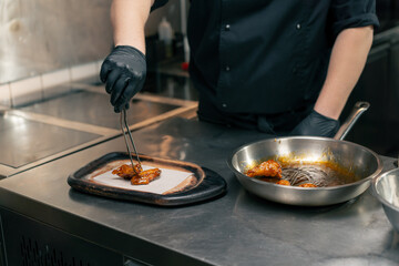 close-up in a professional kitchen the chef puts ready-made chicken wings on wooden tray