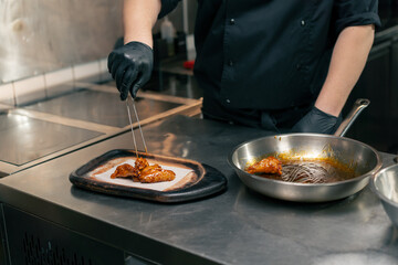 close-up in a professional kitchen the chef puts ready-made chicken wings on wooden tray