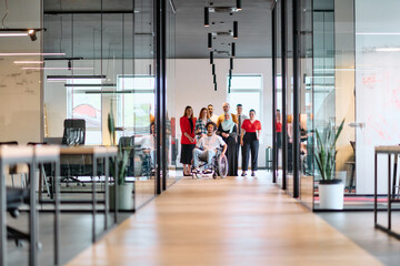 A diverse group of young business people walking a corridor in the glass-enclosed office of a...