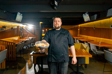 in a restaurant a chef in a black jacket stands with a prepared salad looking at the camera