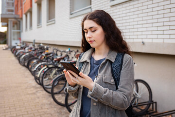 Young Caucasian woman uses her smartphone to rent bike through app. Free municipality transport