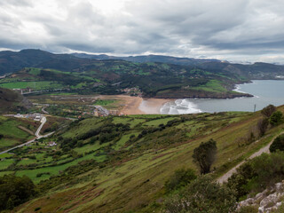 Fototapeta premium a scenic coastal landscape with green hills, a beach, the ocean, and a cloudy sky