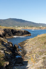 Scenic view of rocky shores, blue waters, distant mountain, clear sky, and bright day with serene natural landscape.