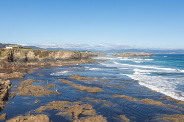 coastline, rocky shores, blue waters, waves crashing, clear sky, distant mountains, peaceful exploration, untouched environment.