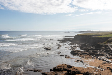 a rocky shoreline with waves crashing under a partly cloudy sky, embodying nature's serene yet untamed beauty