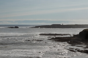 a rocky shoreline with waves crashing under a partly cloudy sky, embodying nature's serene yet...